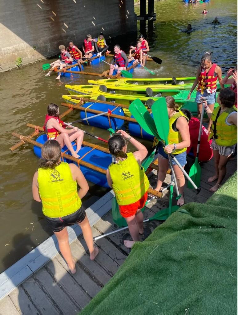 Leerlingen op kajaks en zelfgebouwde vlotten tijdens een teamactiviteit